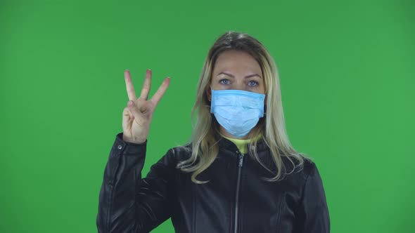 Portrait of Beautiful Young Woman in Medical Protective Face Mask Is Looking at Camera and Shows