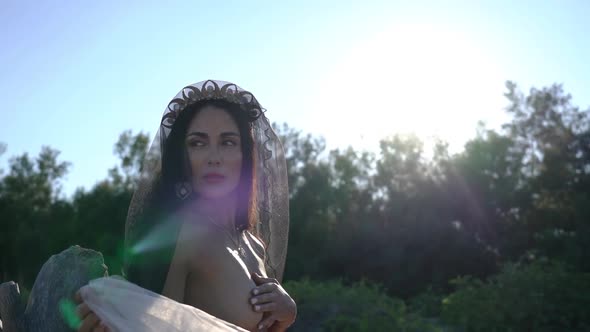 Topless Young Woman in Lacy Veil Stands Against Green Forest