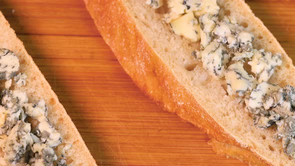 Blue cheese and bread snack over wooden board, rotating. Close up view, macro shot from above.