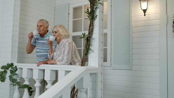 Senior Elderly Couple Drinking Coffee, Looking Ahead in Porch at Home. Mature Family in Own House