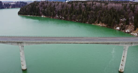 Quadcopter Video of a Bridge Across a River to Hills Covered in Snowy Forest