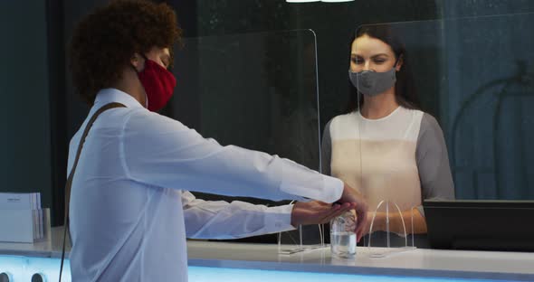 Mixed race man and female receptionist wearing face masks at hotel reception desk