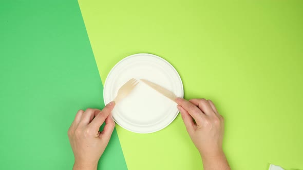  white paper plate and female hands are holding disposable fork and knife 