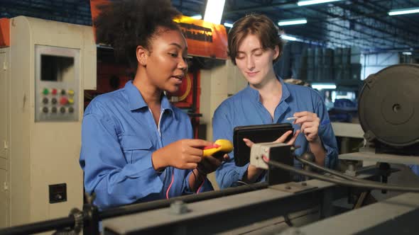 Two professional female engineers inspect machines' electric systems at factory.