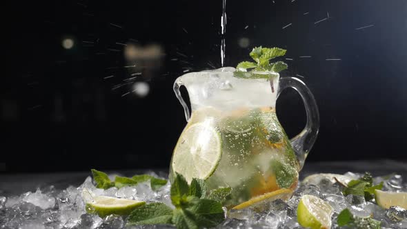 Pouring Pure Sparkling Cold Water Into Transparent Glass Jar with Lime Ice Cubes and Berries