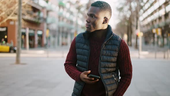 Black Man Browsing Smartphone and Walking in City