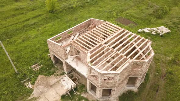 Aerial view of a brick house with wooden ceiling frame under construction.