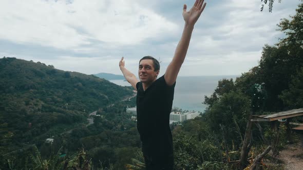 Young Man Traveler Raising His Hands High on Top of the Mountain Above Beautiful Landscape