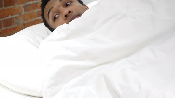 Tired African Man Peeking out from Blanket in Bed