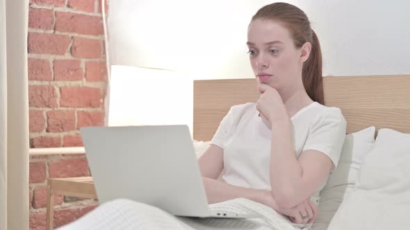 Redhead Young Woman Thinking and Working on Laptop in Bed