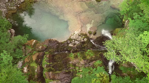 Aerial view of the top of a small waterfall with clean water downhill.