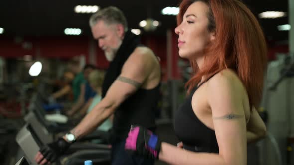 A young woman runs on a treadmill in the gym next to her husband
