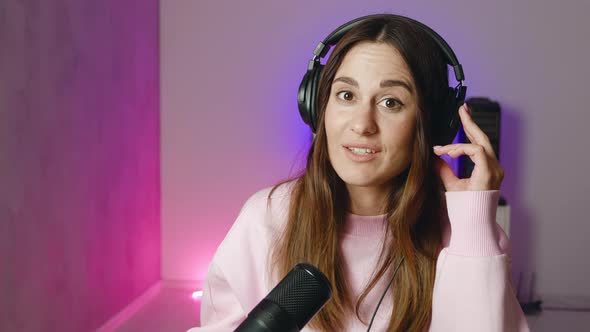 Happy Young Woman Taking Off Headphones Looking at Camera and Talking Smiling While Sitting at Desk