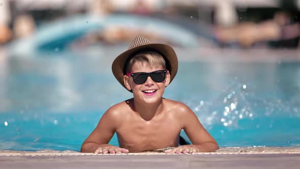 Portrait Laughing Cute Male Kid Vacationer Posing at Swimming Pool Surrounded By Water Splash