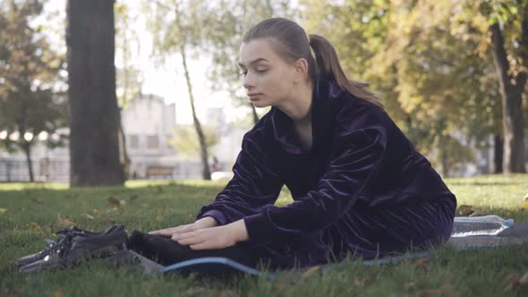 Positive Slim Beautiful Young Sportswoman Touching Toes Stretching on Exercise Mat Outdoors