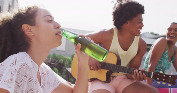 Happy biracial woman drinking beer with diverse friends laughing at pool party