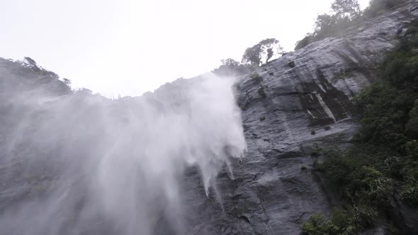 Slow motion shot of waterfall crashing down a cliff face and being blown away in the wind