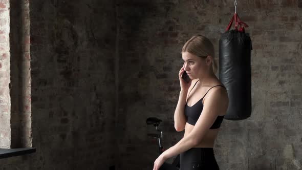 Fitness woman calling mobile phone in gym club. Young woman sitting in gym.