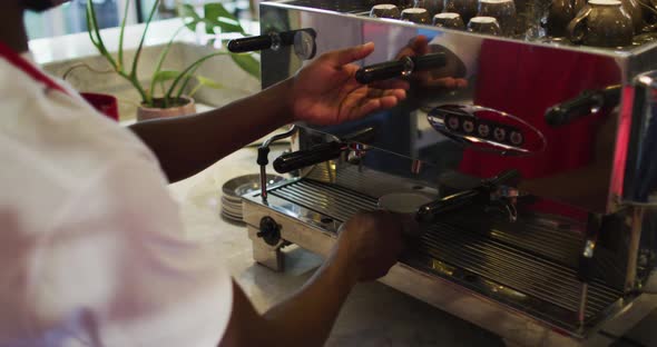 Midsection of african american male barista making coffee in coffee machine