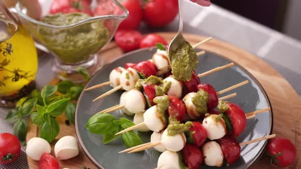 Pouring Pesto Sauce on Caprese Canapes with Cherry Tomatoes and Mozzarella Cheese Balls