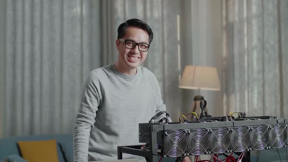 Asian Man Wearing Glasses Smiling To Camera While Using Laptop With Mining Cryptocurrency