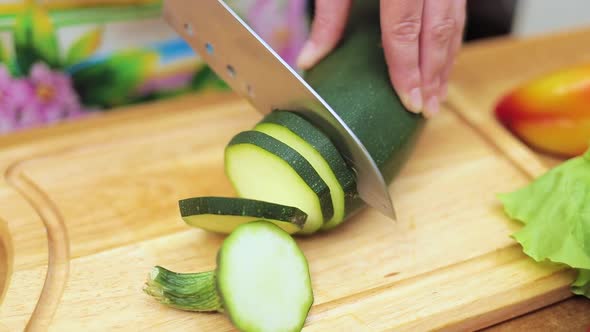 Women's Hands Housewives Cut with a Knife Fresh Zucchini on the Cutting Board of the Kitchen Table