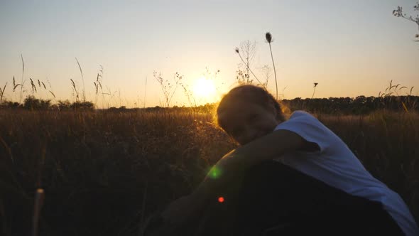 Close Up of Cheerful Little Girl Look Into Camera Sitting in Grass Field at Sunset Time