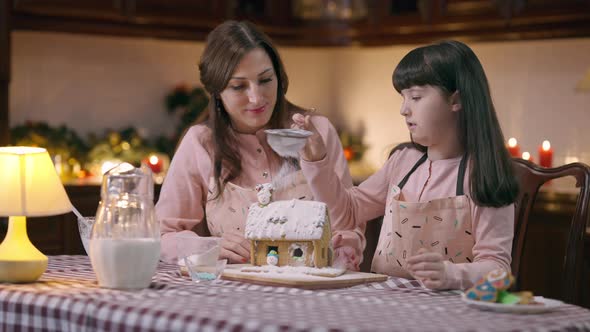 Girl Sprinkling Powdered Sugar on Ginger House in Kitchen at Home