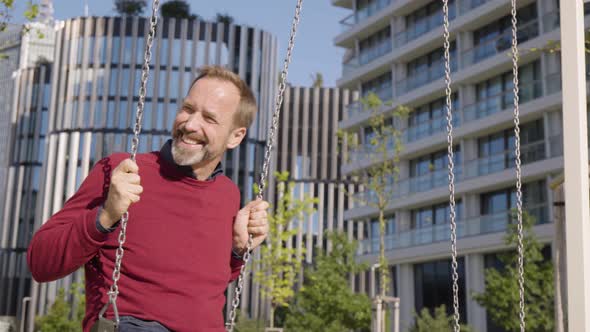 A Middleaged Handsome Caucasian Man Swings on a Swing with a Smile and Looks Around