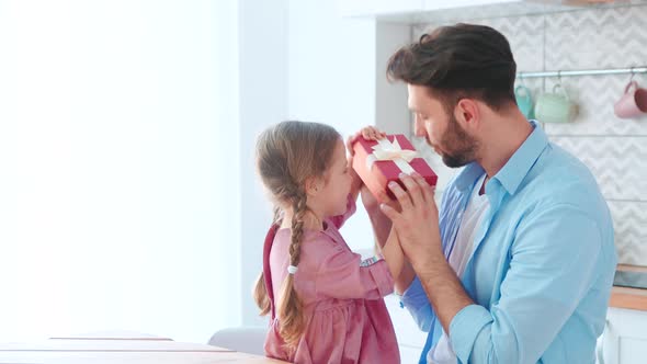 Young parent giving a present to his little daughter in a home interior