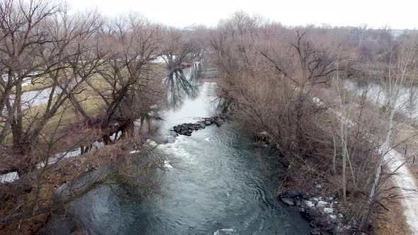 Small river dam and rapids on scenic, idyllic, willow tree lined flowing river in winter in rural co