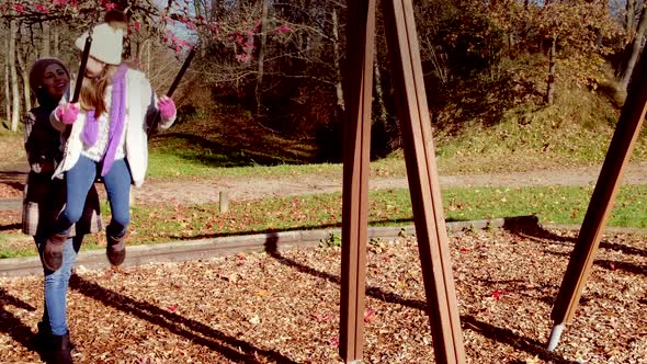 Mother and daughter play on playground swing