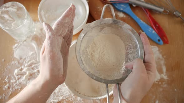 Top View of Young Woman Shaking Sieve for Sifting Flour While Making Dough