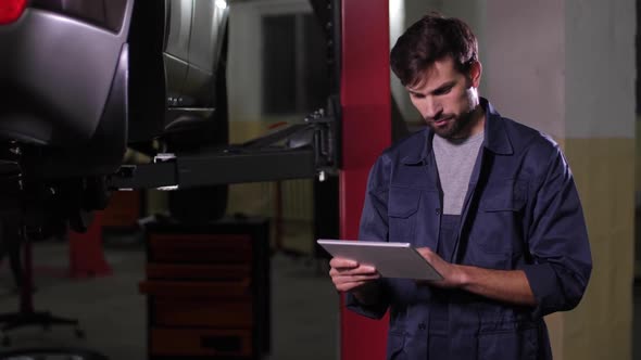 Repairman Working on Tablet in Car Workshop