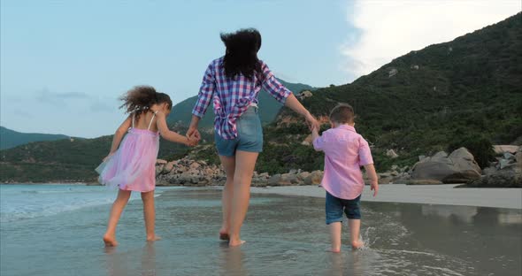 Young Family, Mother and Children Are Walking Along the Coast. Happy Family Walking on Sea Coast.