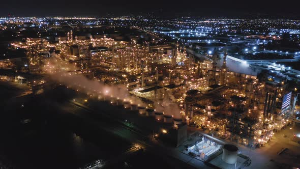Working Illuminated Petroleum Refinery in Front of Panoramic City View at Night. Aerial Shot. alt