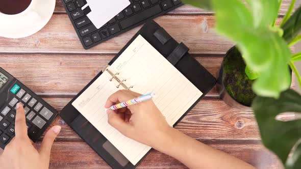 Top View of Women Hand Using Calculator and Writing on Notepad on Office Desk