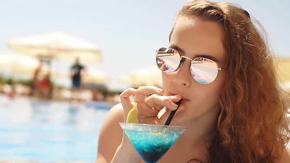 Beautiful Young Woman Relaxing Near Swimming Pool with Cocktail. Slow Motion
