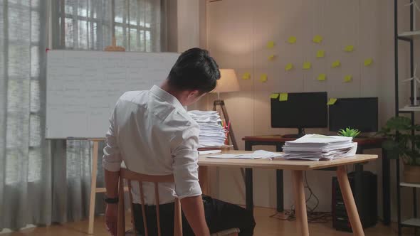 Back View Of Asian Man Leaning On The Chair And Sleeping While Working Hard With Documents