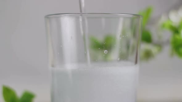 Pouring cold transparent carbonated soft drink into glass, green background