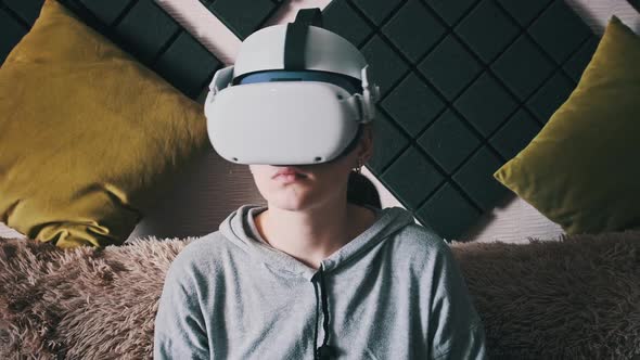 Young Woman Sitting on Sofa Playing Game Using VR Helmet Indoor at Home