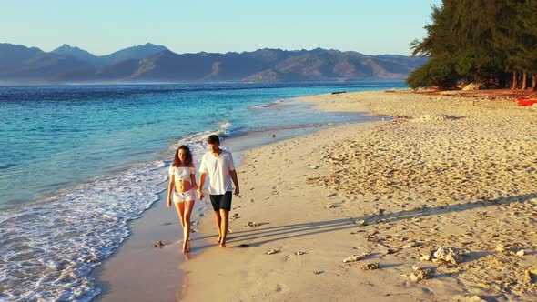 Beautiful young couple walking barefoot on sandy beach washed by sea waves with mountains tropical i