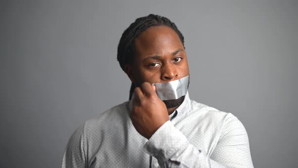 AfricanAmerican Guy Taking Tape Off His Mouth on Grey Background