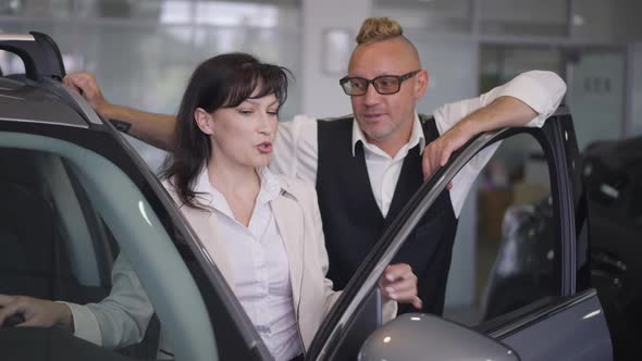 Loving Adult Caucasian Couple Standing in Car Dealership Discussing Vehicle Choice
