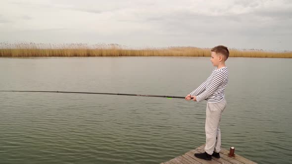 A Boy in Striped Clothes Catches a Fish on Fishing Rod