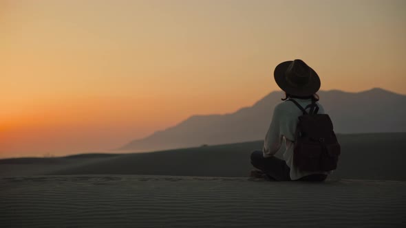 Attractive girl with a backpack sitting in a lotus position on the sand