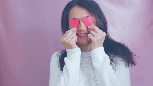 Smiling Funny Young Brunette in a White Sweater Smiles Blinks and Waving Red Hearts on a Pink