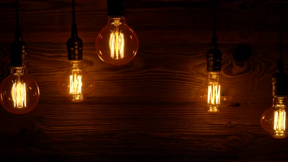 Vintage Light Bulbs Slowly Lit On Old Wood Background.