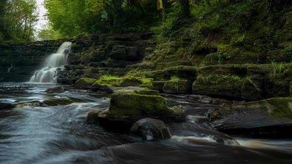 Panorama time lapse of spring forest cascade waterfall surrounded by trees with rocks in the foregro