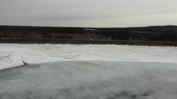 Aerial fly over edge of frozen dam into winter forest